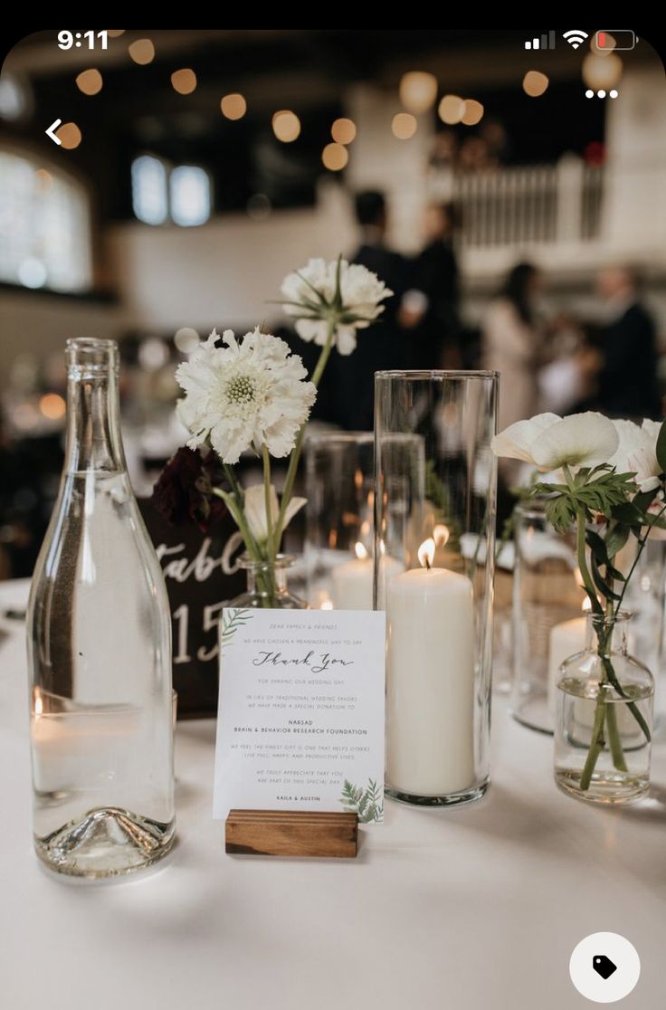 the table is set with candles and vases filled with white flowers, greenery, and cards