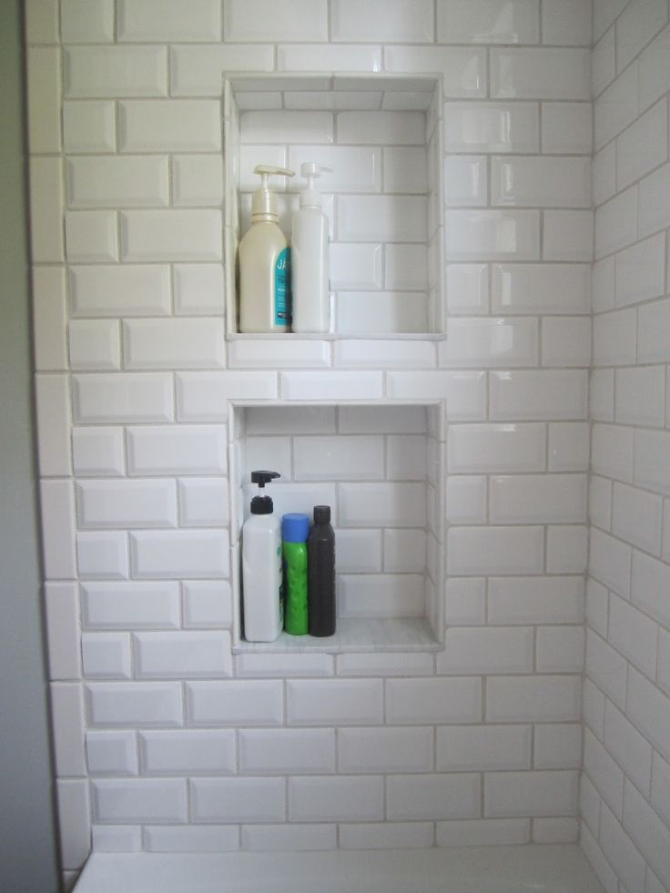 a white tiled shower with shelves and soaps on the wall next to each other