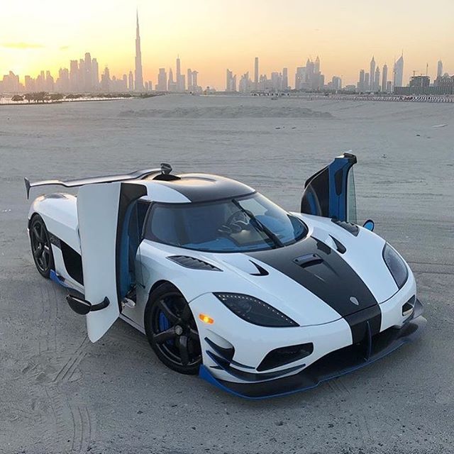 a white and black sports car parked on the beach with city skyline in the background