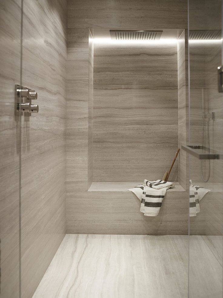 a bathroom with a wooden floor and white tile on the walls, along with a glass shower door