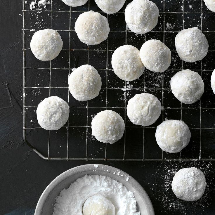 several balls of powdered sugar on a cooling rack next to a bowl of powder