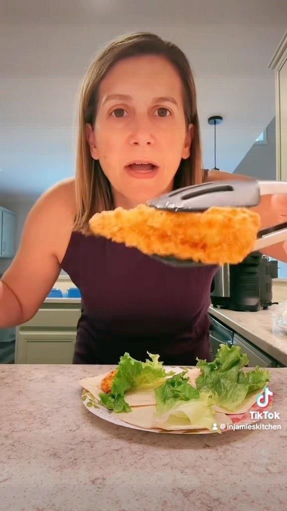 a woman is holding up a slice of pizza on a plate with lettuce