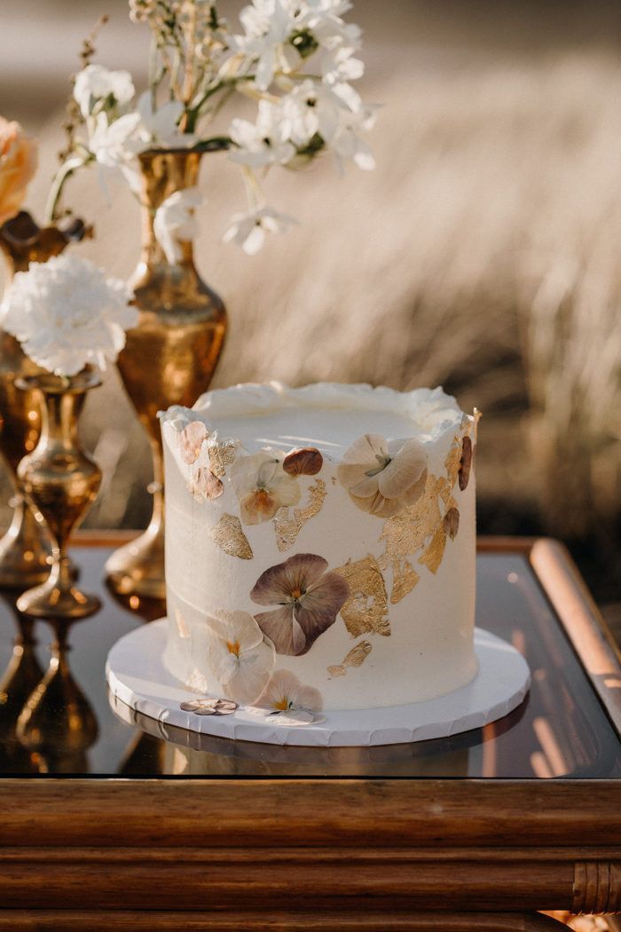 a white cake sitting on top of a table next to two vases filled with flowers