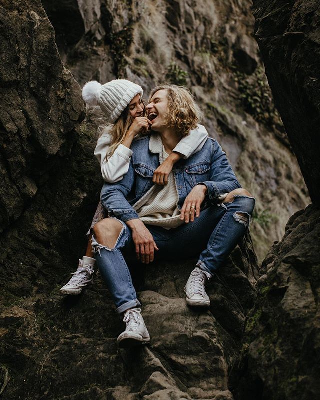 two people are sitting on some rocks and one is kissing the other's cheek