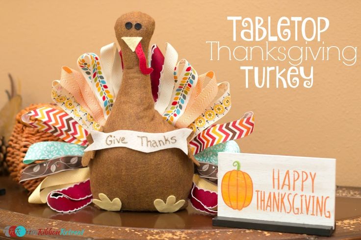 a stuffed turkey sitting on top of a table next to a sign that says happy thanksgiving