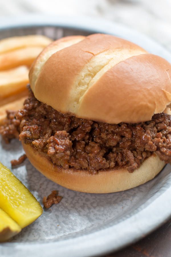 a sloppy joe sandwich on a plate with fries and pickle slices next to it