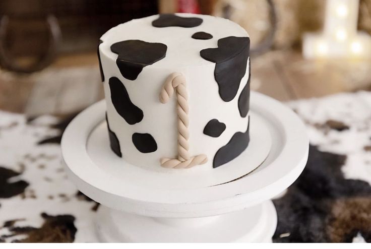 a cake with black and white designs is on a stand in front of a cow print tablecloth