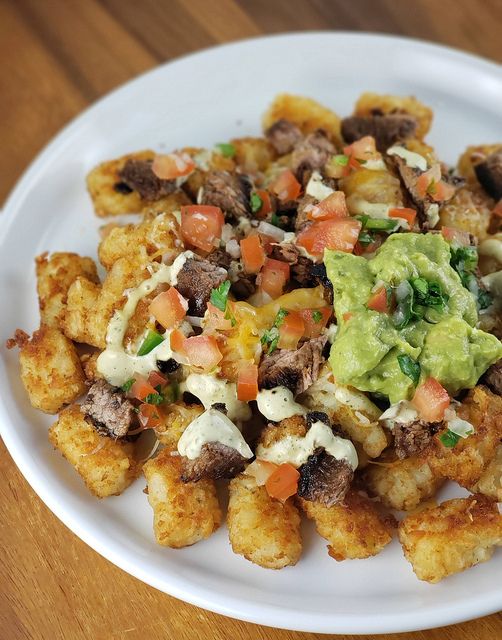 a white plate topped with tater tots covered in guacamole and salsa