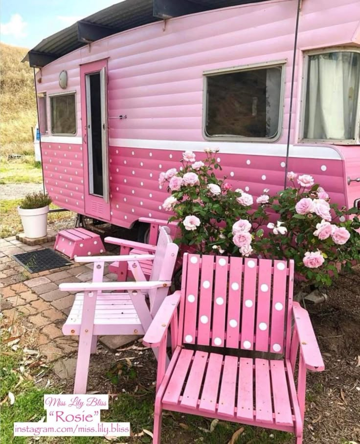 a pink and white trailer is sitting in the grass with two chairs next to it