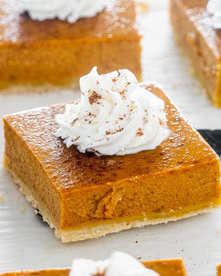 several pieces of pumpkin pie with whipped cream on top, sitting on a white surface