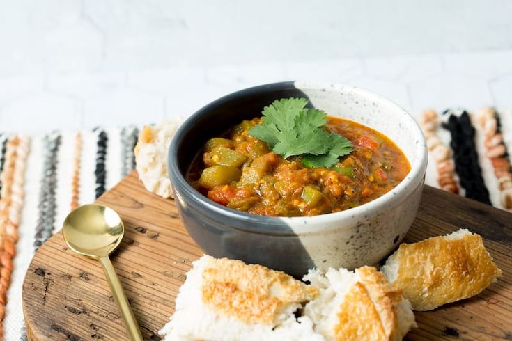 a bowl of chili and bread on a wooden cutting board with a spoon next to it