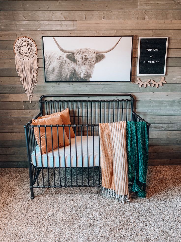 a baby crib in front of a wall with pictures on it and blankets draped around the crib