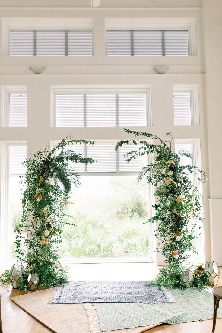 an indoor ceremony with greenery and flowers on the altar, surrounded by large windows