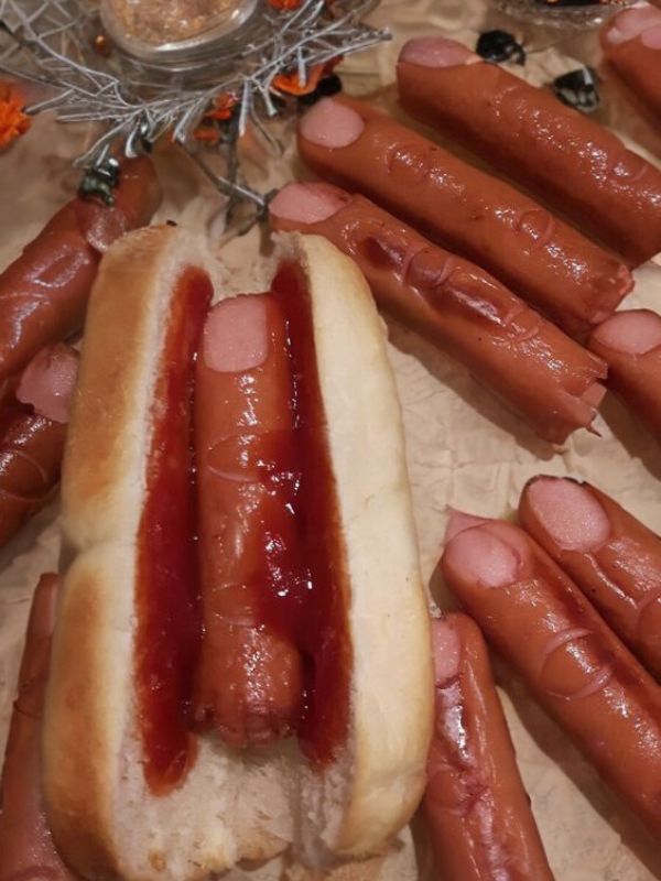 two hotdogs with ketchup on them and some buns in the background