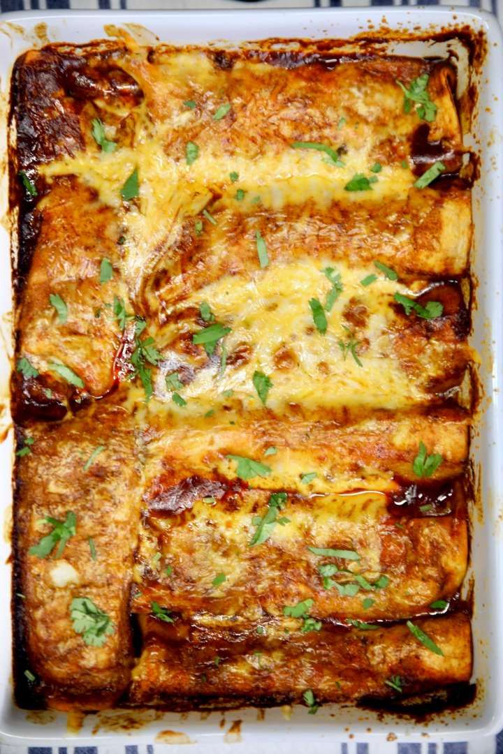 a casserole dish with meat, cheese and parsley in it on a blue checkered table cloth