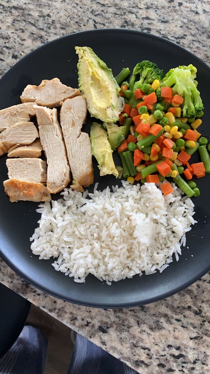 a black plate topped with rice, meat and veggies