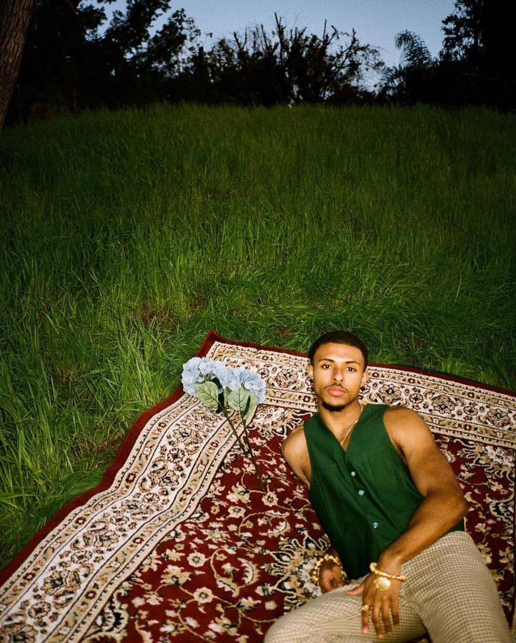 a man sitting on top of a rug in the grass