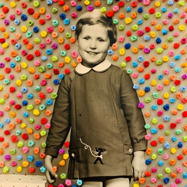 a young boy standing in front of a wall covered with multicolored flowers and buttons