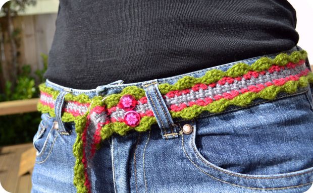 a woman is wearing a crocheted belt with pink flowers on the bottom and green trim