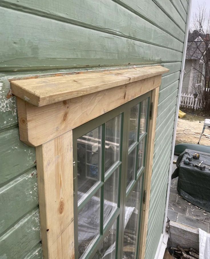 a wooden window frame on the side of a house with green siding and wood trim