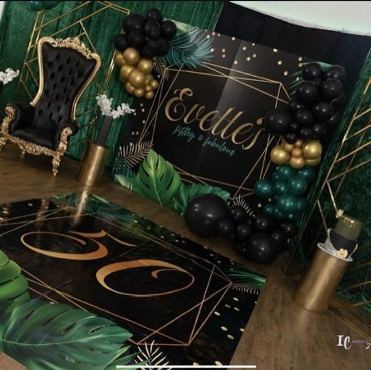 a room decorated with black and gold balloons, green curtains, and palm leaf decorations