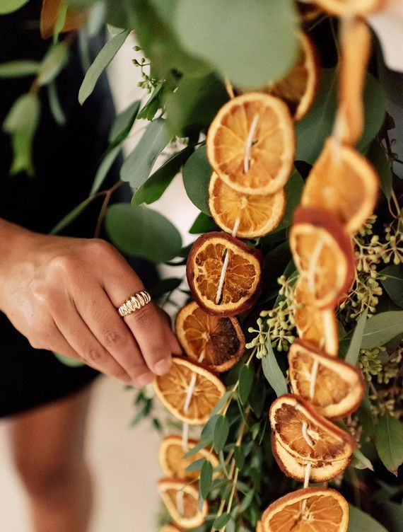 a close up of a person holding an orange on a table with leaves and flowers