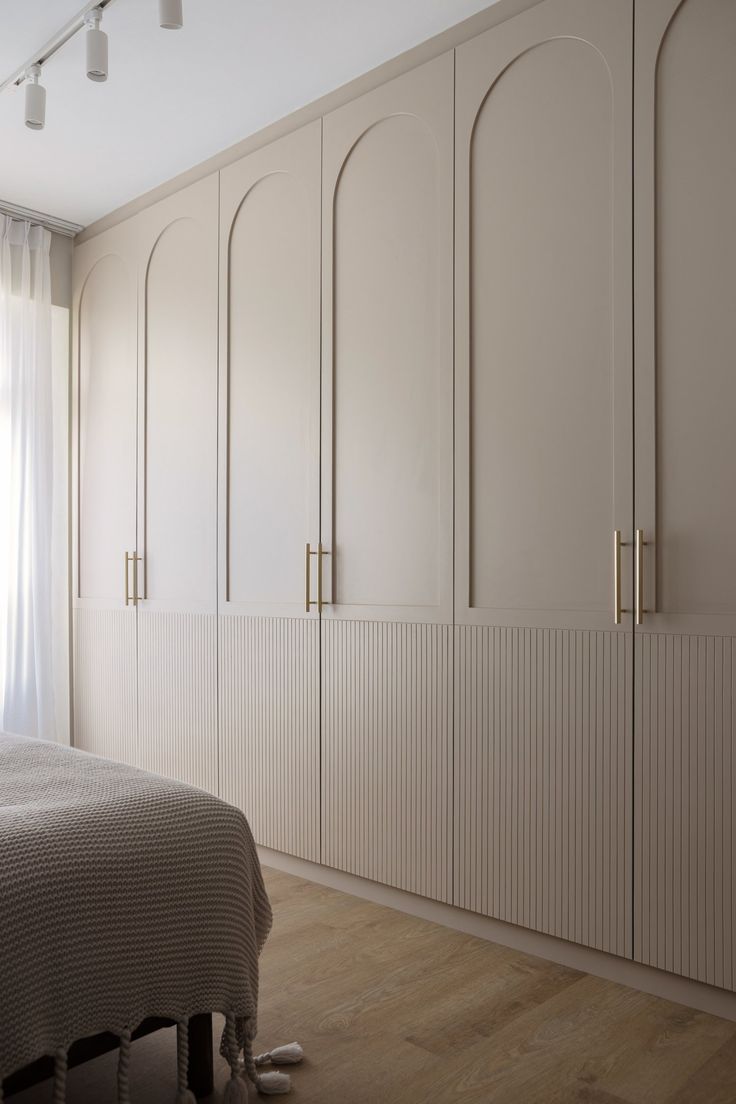 a bedroom with white cabinets and a bed in the corner, along with wooden flooring