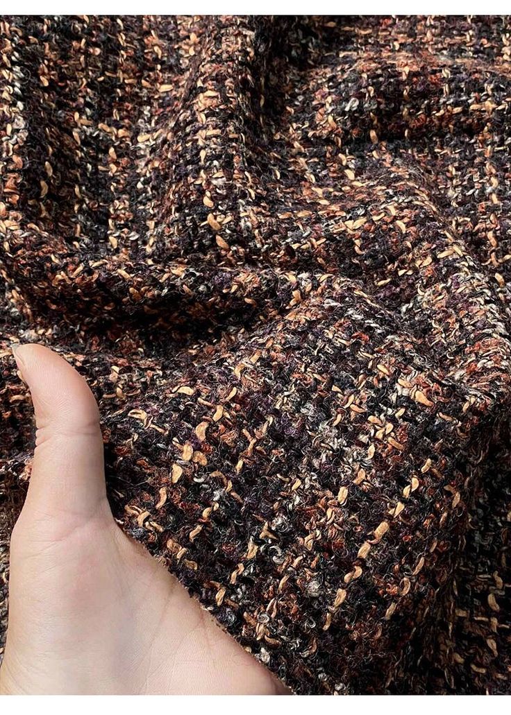 a hand is pointing at a brown and black tweed fabric