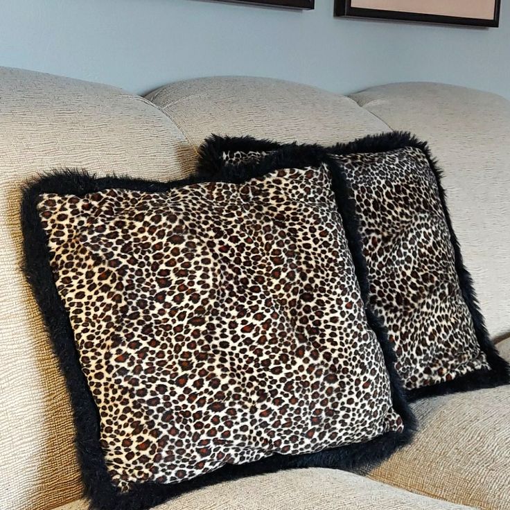 two leopard print pillows sitting on top of a couch next to a framed photo and another animal print pillow