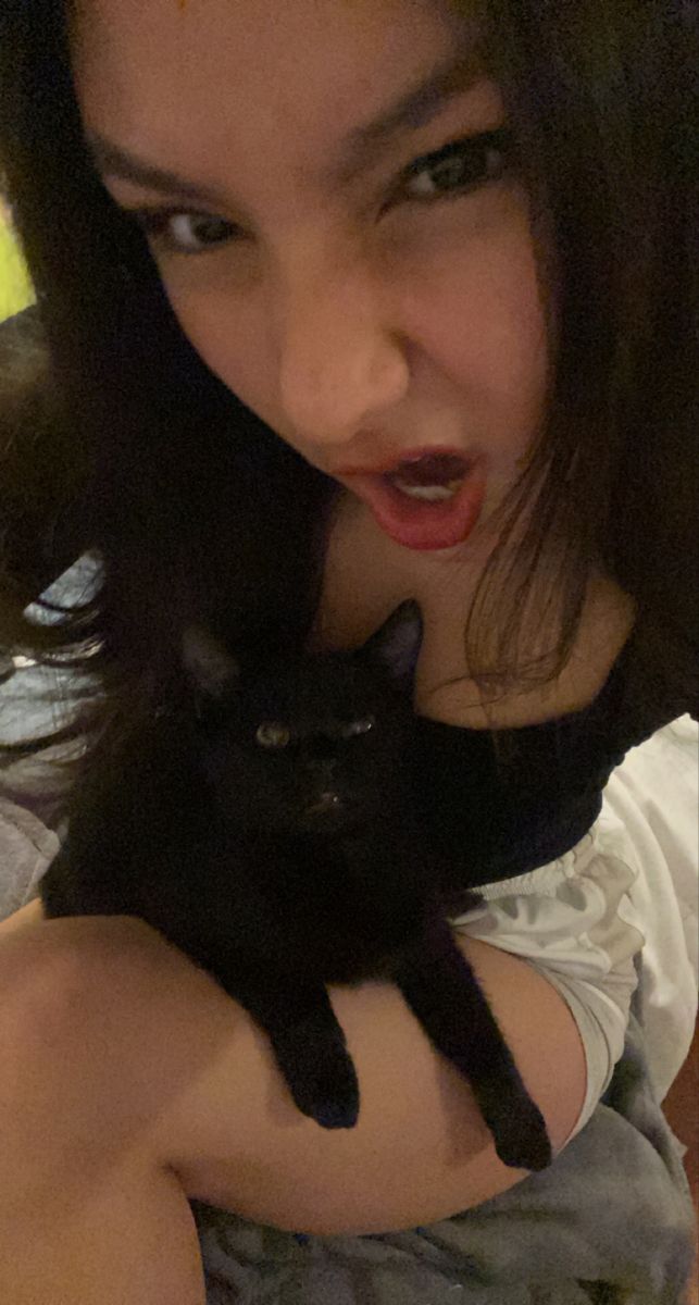 a woman is holding a black cat in her arms while she looks at the camera