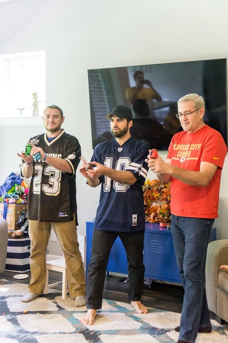 three men standing in a living room holding remotes