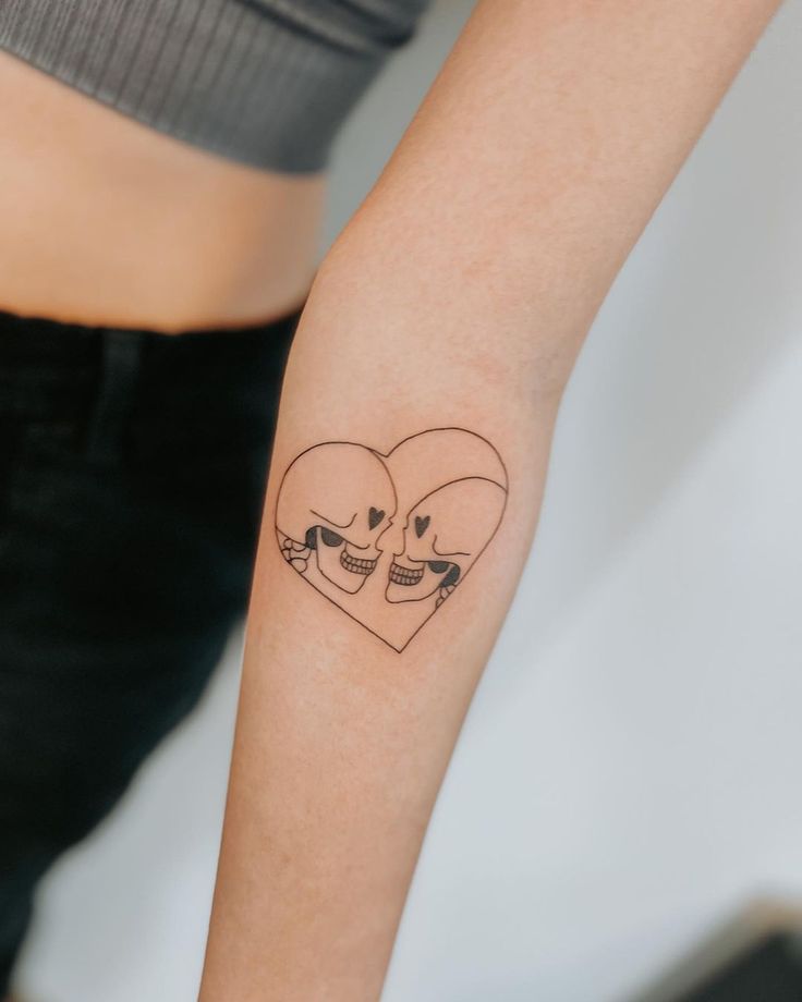 a couple of skulls in the shape of a heart tattoo on the left forearm and arm