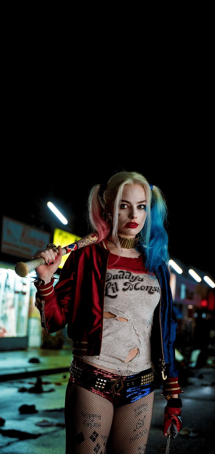 a woman with blue hair and makeup is holding a knife in her hand while standing on the street