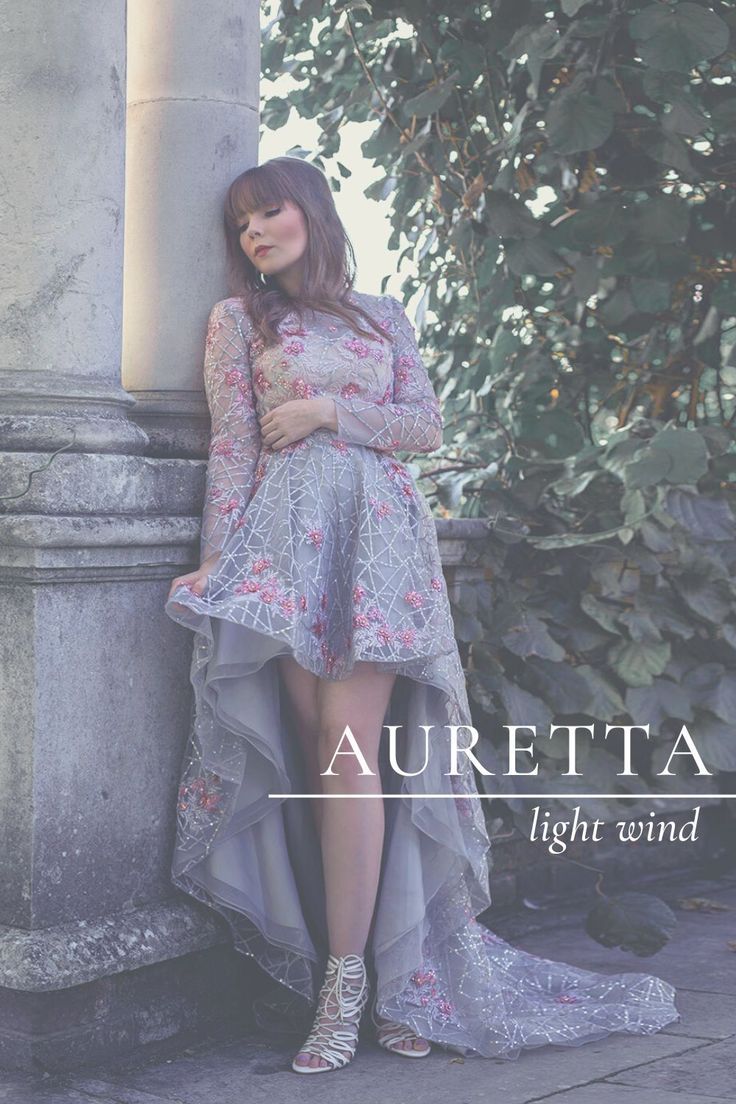 a woman leaning against a pillar wearing a dress with flowers on it and the words auretta light wind