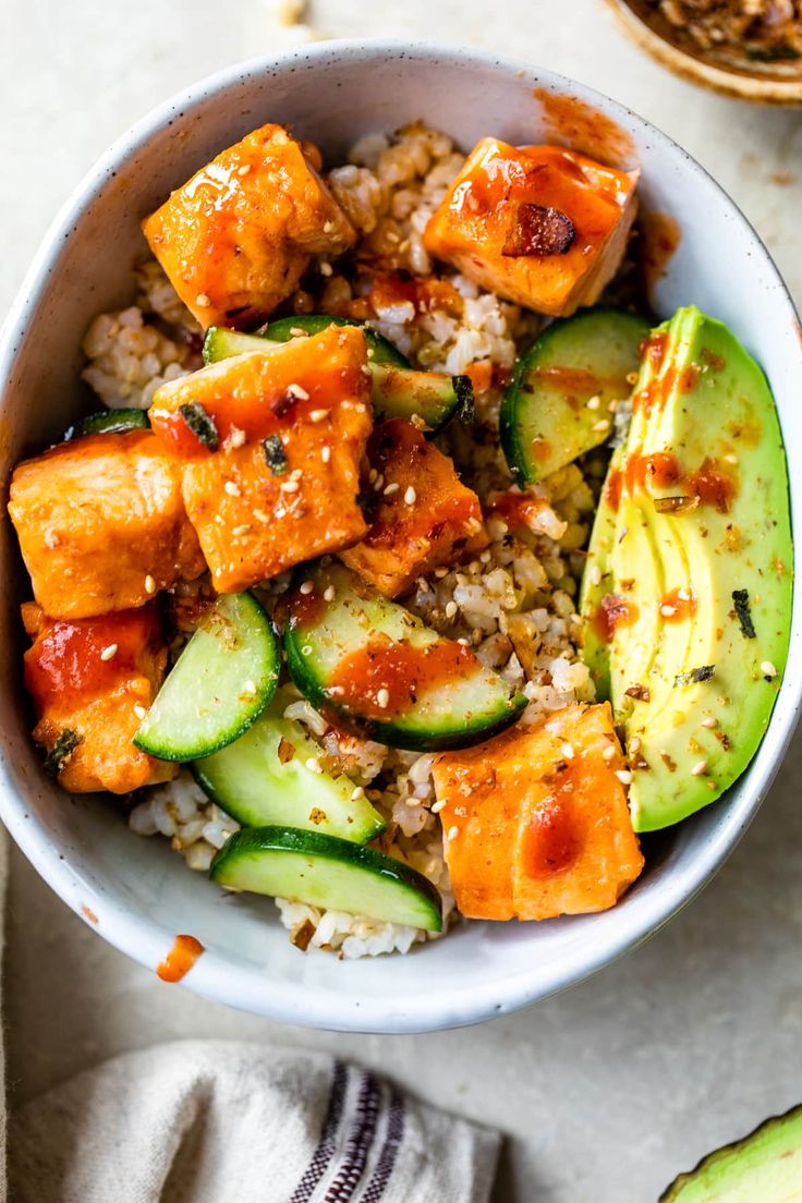 a bowl filled with rice, cucumber and chicken next to an avocado