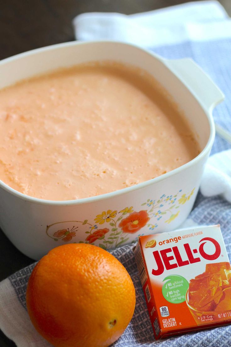 an orange sitting next to a bowl of jello and a small box of candy