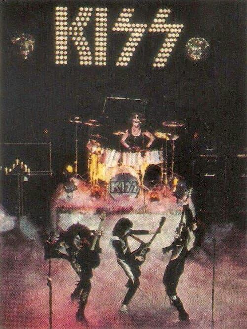 the band kiss performing on stage in front of microphones