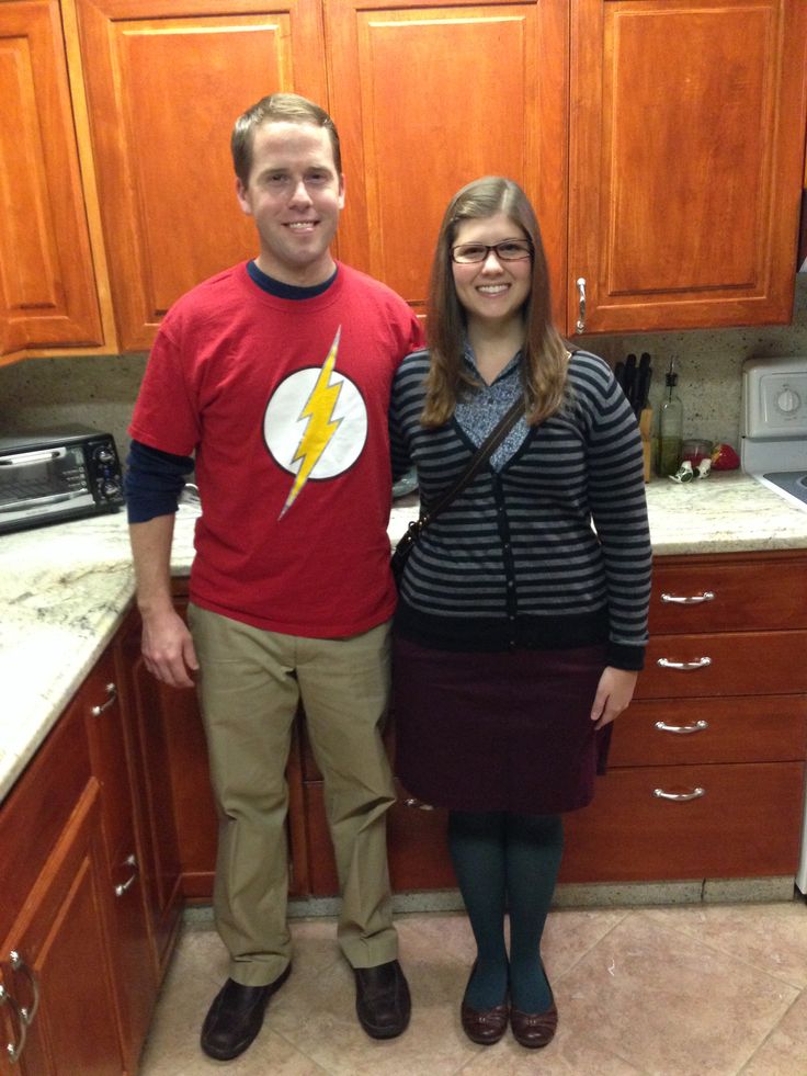 a man and woman standing next to each other in a kitchen with wooden cupboards