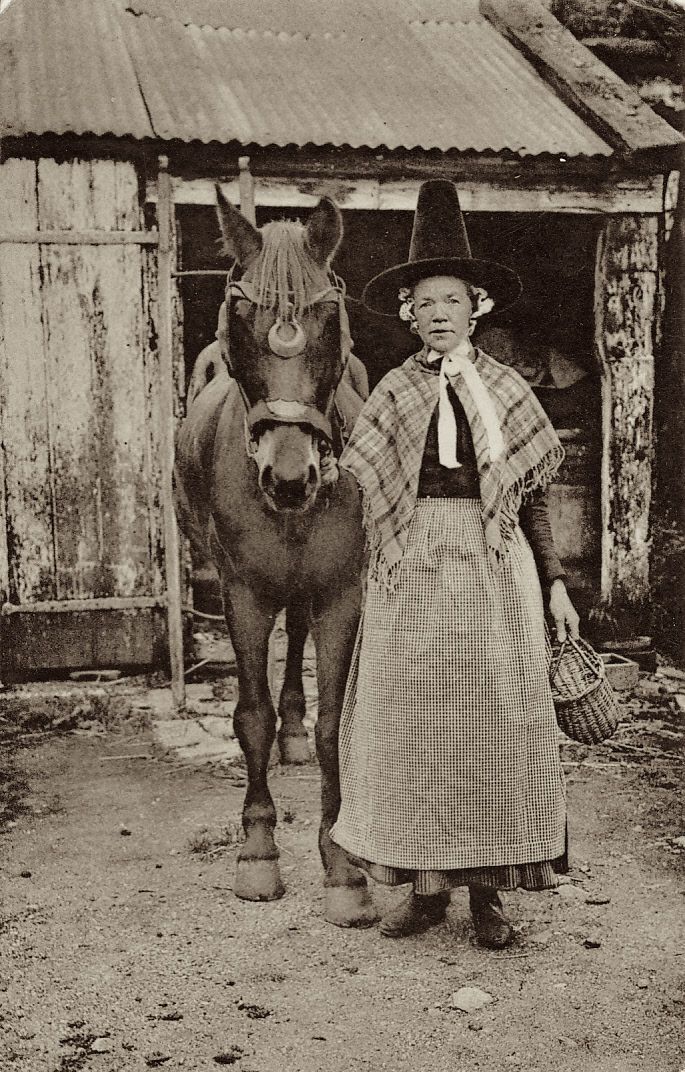 an old black and white photo of a woman standing next to a horse in front of a barn