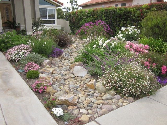 a garden with rocks and flowers in front of a house