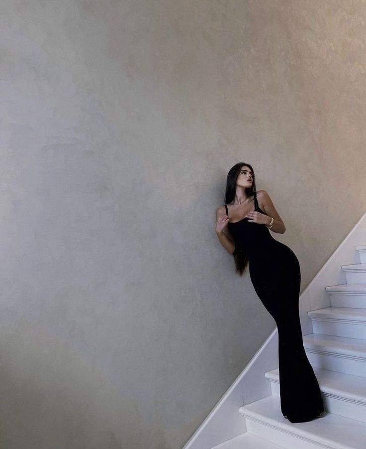 a woman in a long black dress standing on the stairs