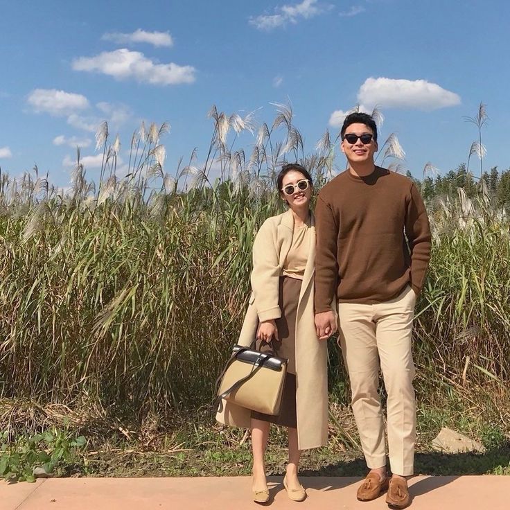 a man and woman standing next to each other in front of a field with tall grass