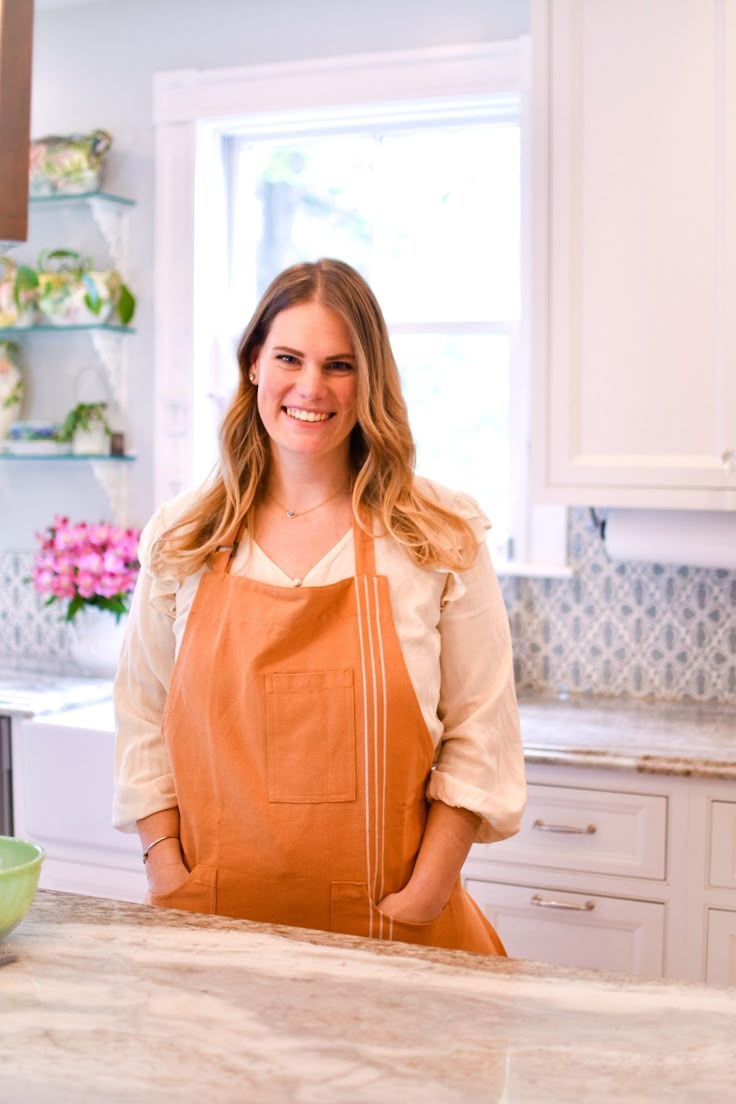 a woman in an orange apron is standing at the kitchen counter with her hands on her hips