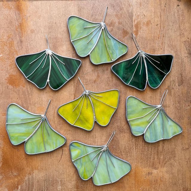 six green and yellow leaf shaped glass ornaments on a wooden surface with string attached to them