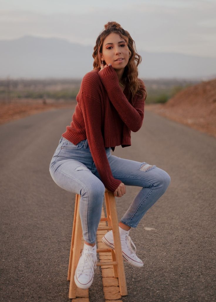 a woman sitting on top of a wooden ladder in the middle of an empty road