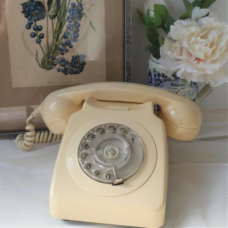 an old fashioned phone sitting on a table next to a vase with flowers in it