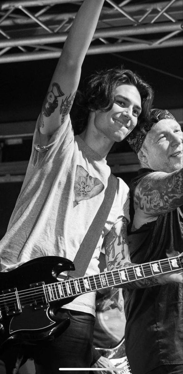 two men with tattoos on their arms and one holding a guitar in the other hand