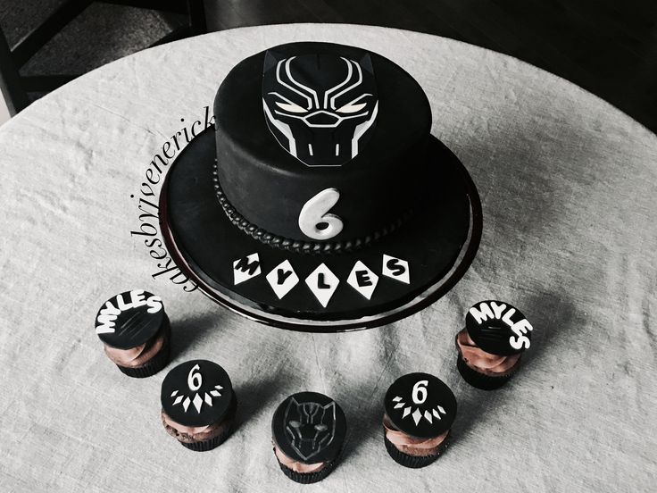 a black cake sitting on top of a table next to cupcakes and decorations