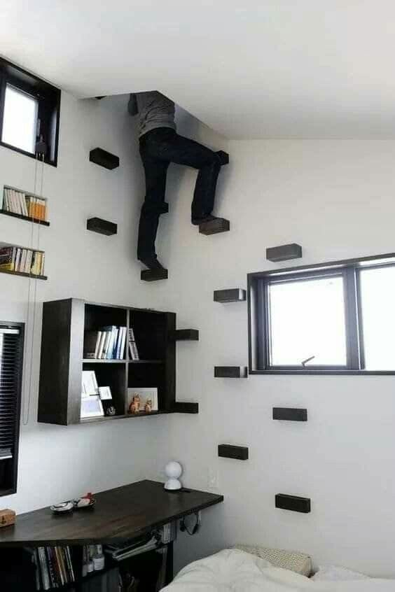 a man is hanging upside down from the ceiling above a bed in a room with bookshelves