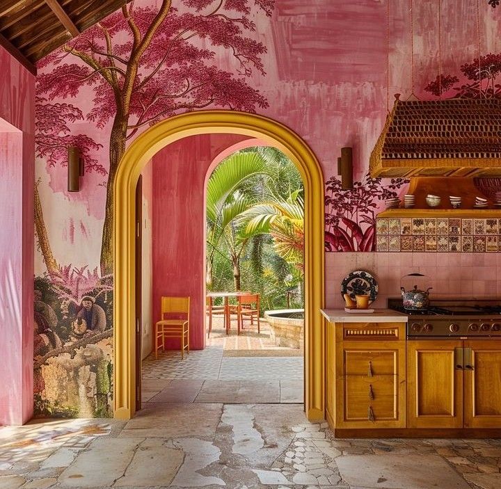 an archway leads into a pink kitchen with trees painted on the walls and flooring